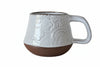 White ceramic mug with embossed design on a white background